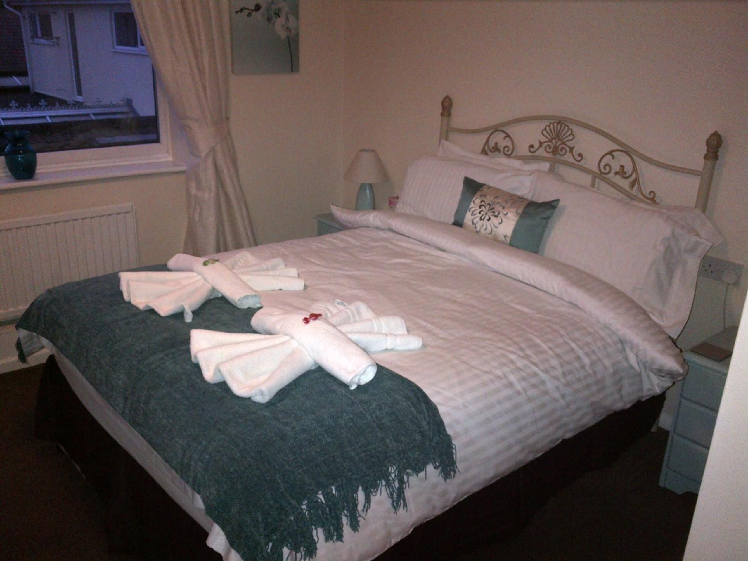 A neatly made bed with towels, a window with curtains, and a wall with a floral painting.