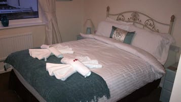 A neatly made bed with towels, a window with curtains, and a wall with a floral painting.