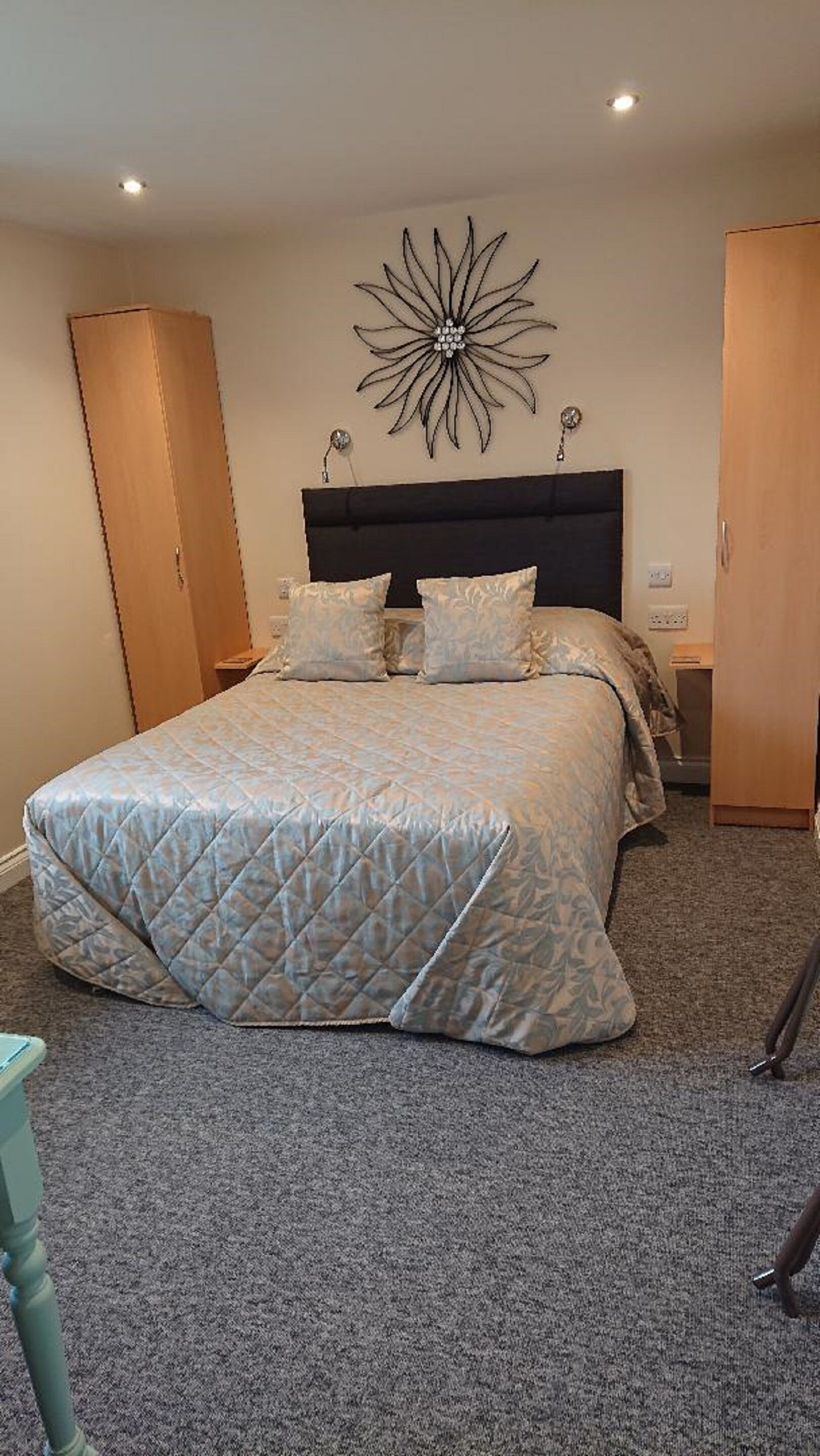 A bedroom with a large bed, a dark headboard, a decorative wall piece, and wooden wardrobes.