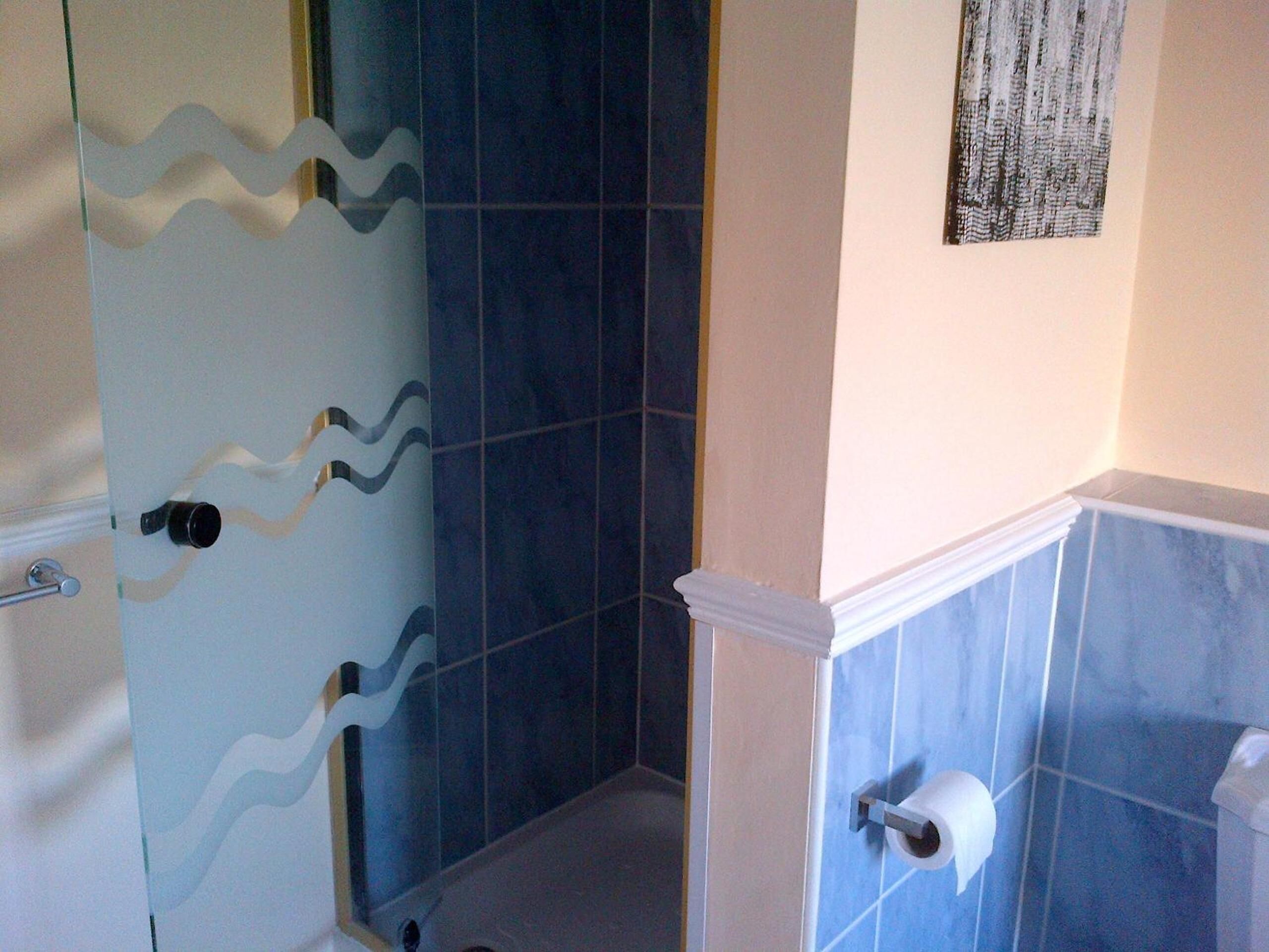 Un baño con azulejos azules, una puerta de ducha de vidrio, un dispensador de papel higiénico y un perchero para toallas.