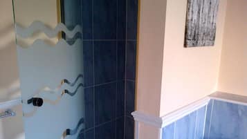 Un baño con azulejos azules, una puerta de ducha de vidrio, un dispensador de papel higiénico y un perchero para toallas.