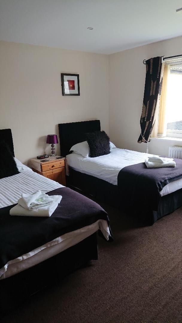 A hotel room with two beds, a nightstand, a lamp, and a window with curtains.