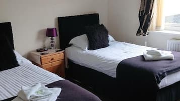 A hotel room with two beds, a nightstand, a lamp, and a window with curtains.