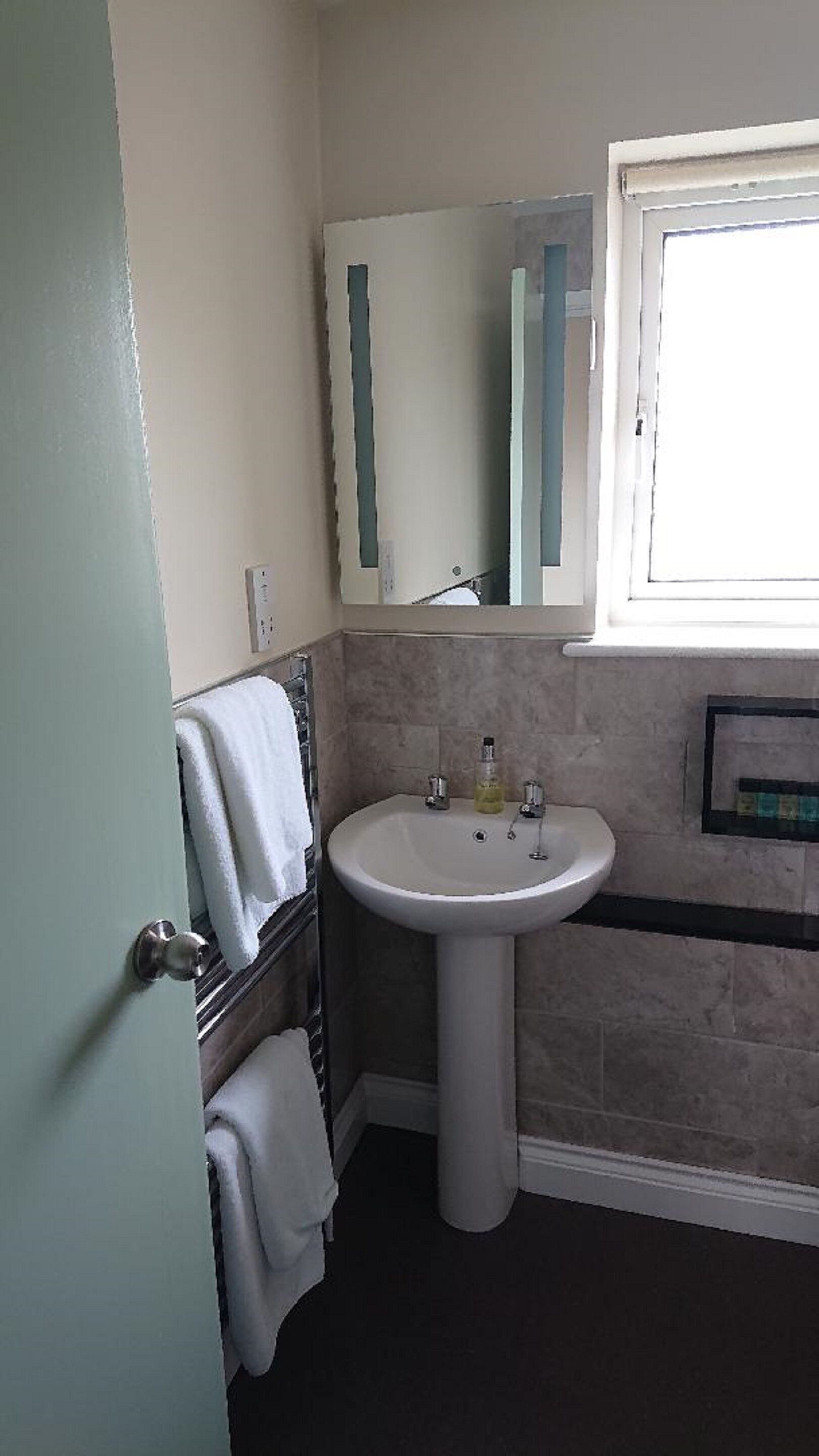 Un baño con lavamanos pedestal, un espejo encima y una ventana a la derecha.
