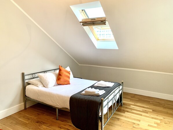 A small, single-bed room with a skylight, wooden flooring, and a simple metal bed frame.