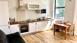 Eine kleine Küche mit weißen Schränken, einer Holzausziehtischplatte und einem Essbereich mit Tisch und Stühlen.