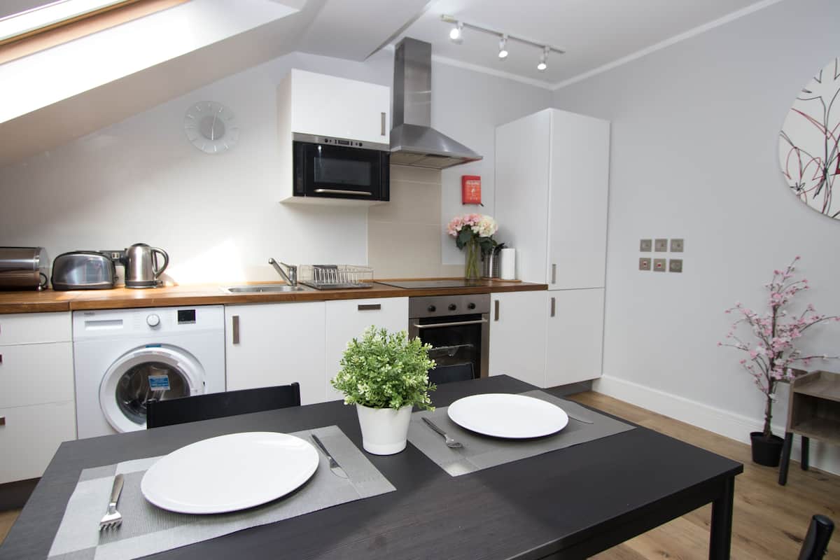 Een moderne keuken met een vaatwasser, oven, magnetron en een eethoek met een tafel gedekt voor twee personen.