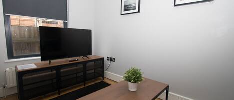 A modern living room with a flat-screen TV, a wooden coffee table, a potted plant, and two framed pictures on the wall.