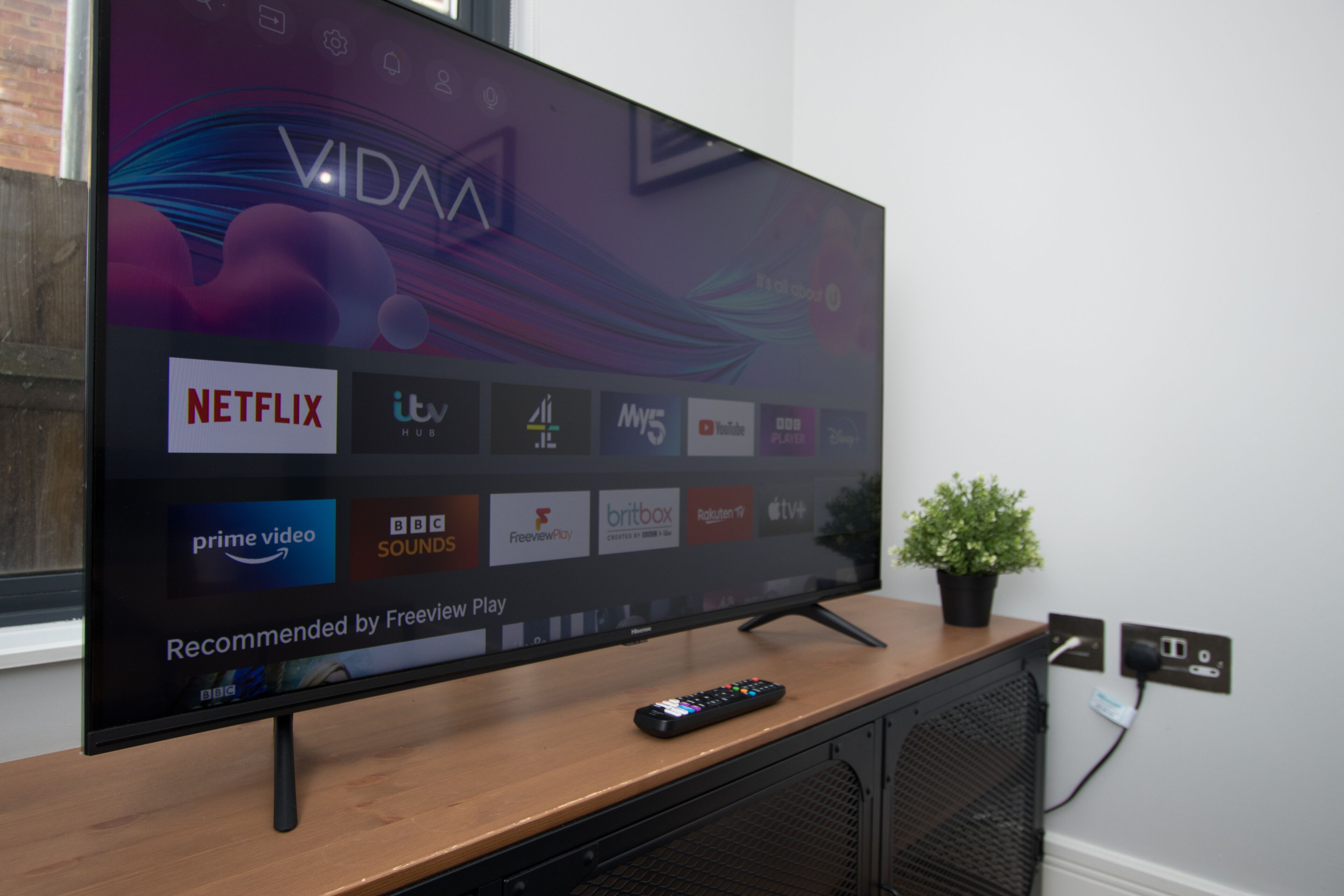 Un televisor de pantalla plana sobre un atril de madera, con un control remoto a su lado.