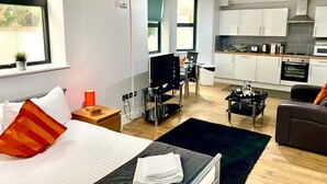 Ein modernes Hotelzimmer mit Bett, Fernseher, Schreibtisch, Sessel, einer Couch und einer Küchenzeile.