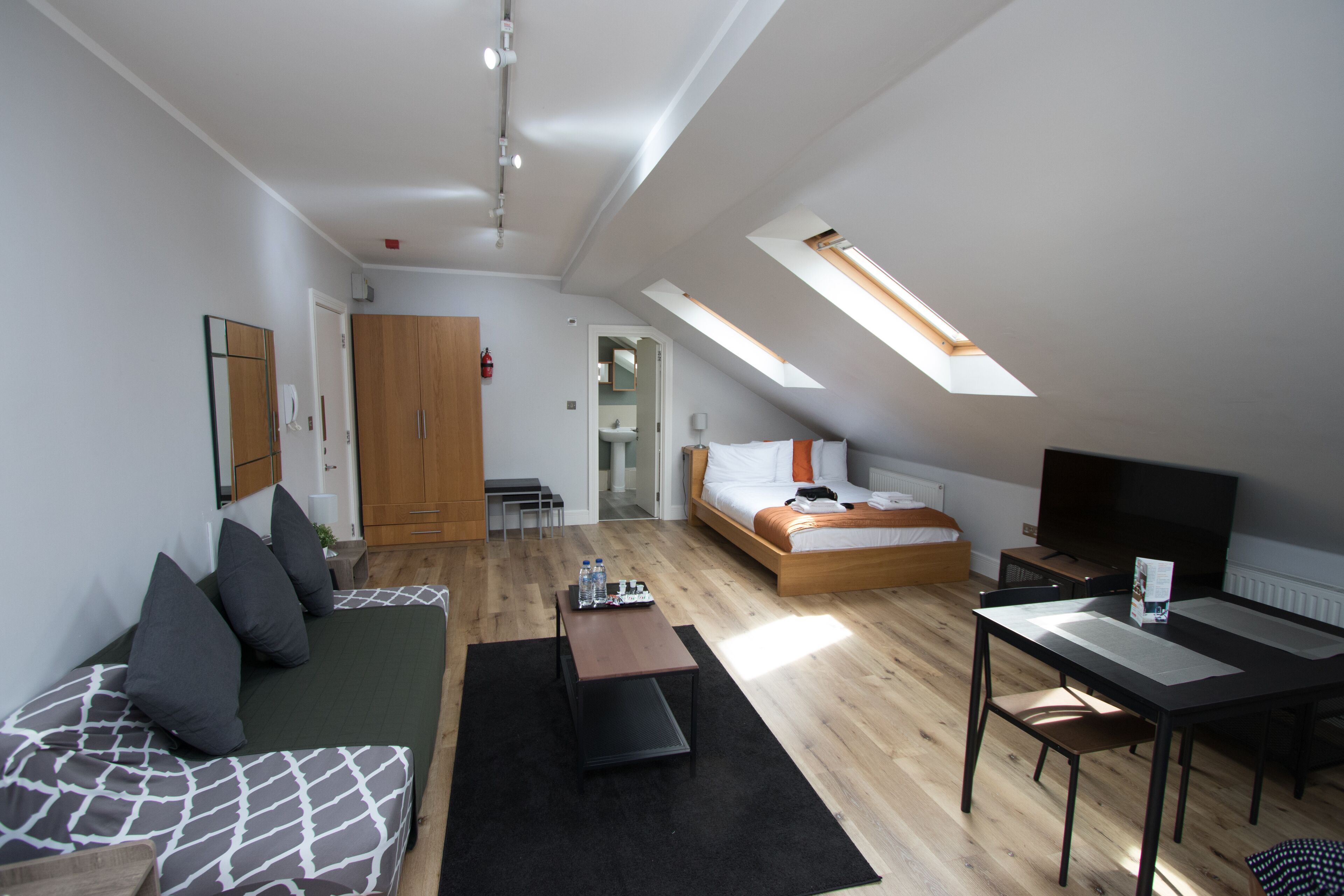 A modern loft bedroom with a skylight, a bed, a TV, and a dining area.