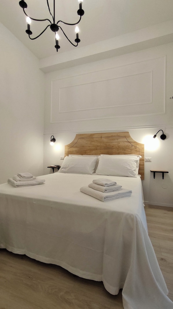 A neatly made bed with white linens, a wooden headboard, and two wall-mounted nightstands with lamps.