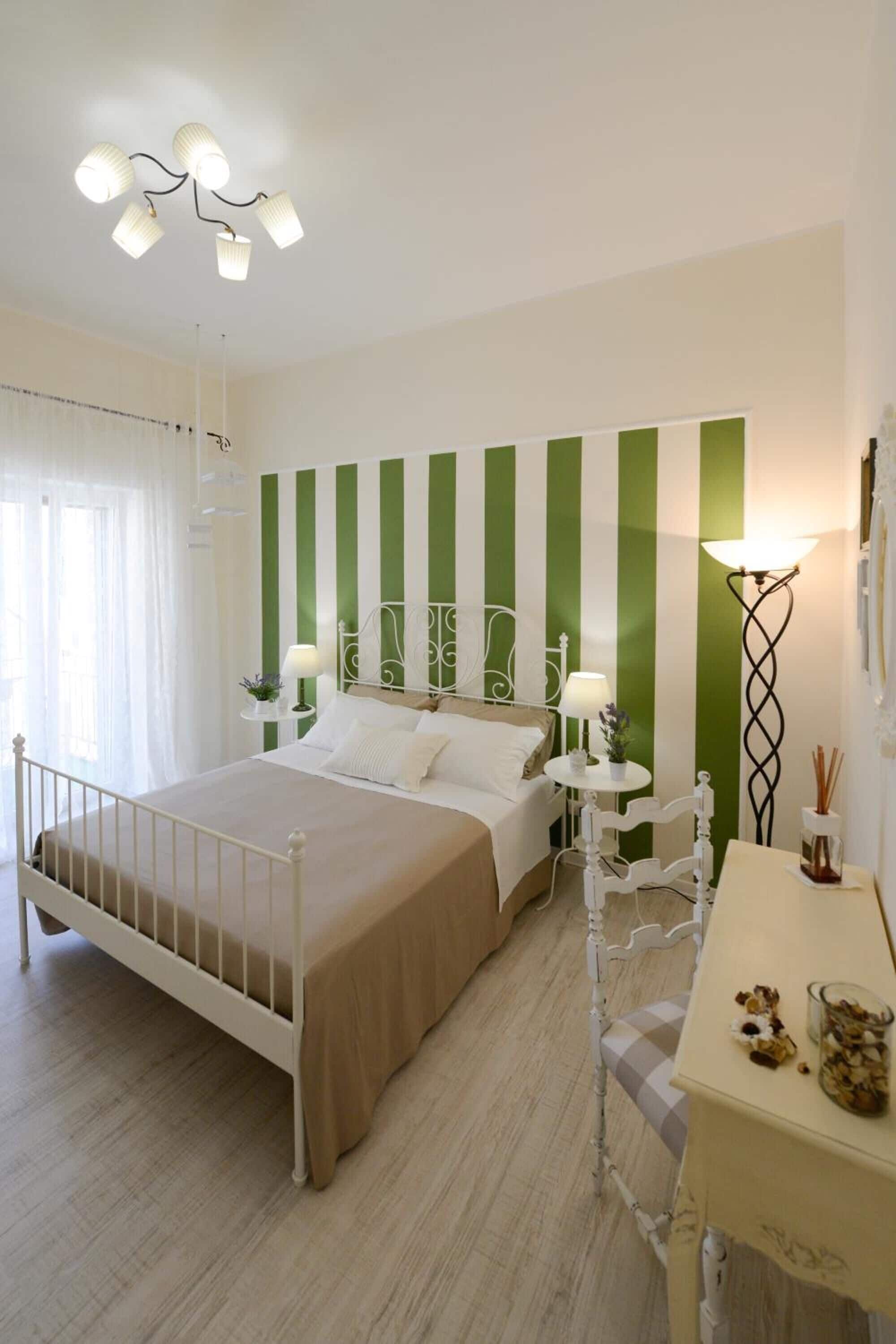 A bedroom with a bed, bedside tables, a lamp, and a wall with vertical stripes.