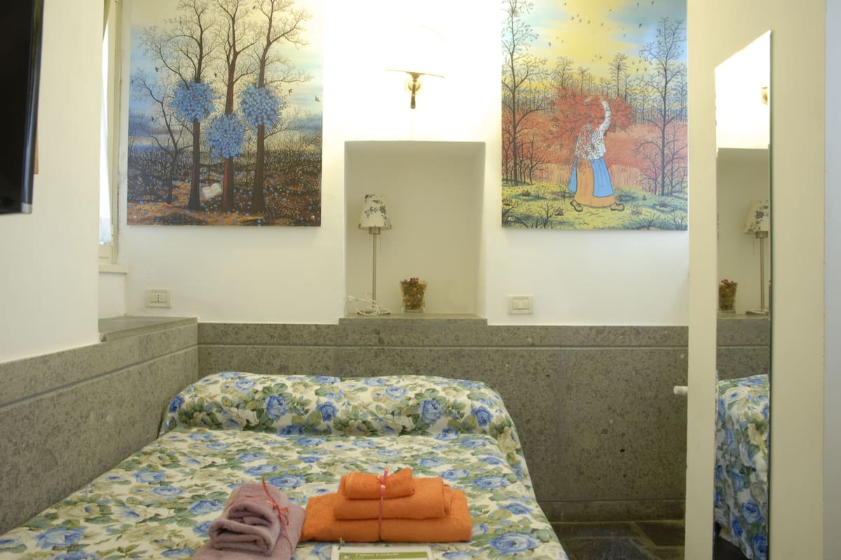 A hotel room with a bed, a painting on the wall, and a lamp.