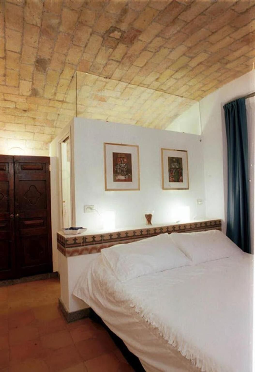 A room with a bed, a wooden wardrobe, and two framed pictures on the wall.