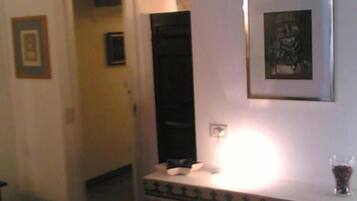 Una habitación de hotel con una cama, una mesita de noche con una lámpara, un cuadro enmarcado en la pared y una puerta que da a otra habitación.