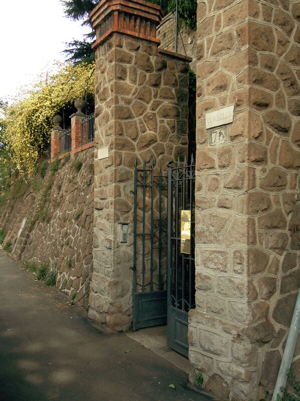 A stone building with a metal gate, a sign with the number 175, and a staircase leading up to a balcony. - Villino Corbelli (Rome)