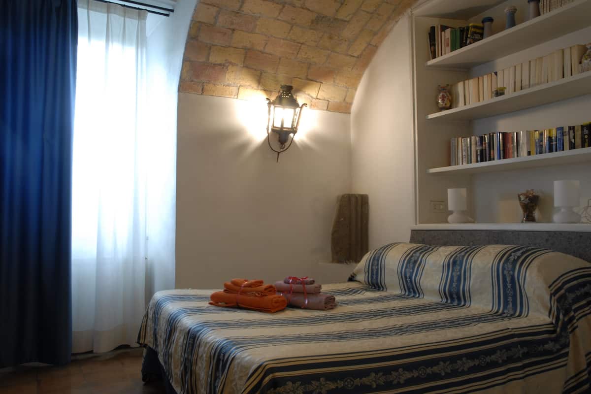 A bedroom with a bed, a bookshelf, and a wall-mounted light fixture.