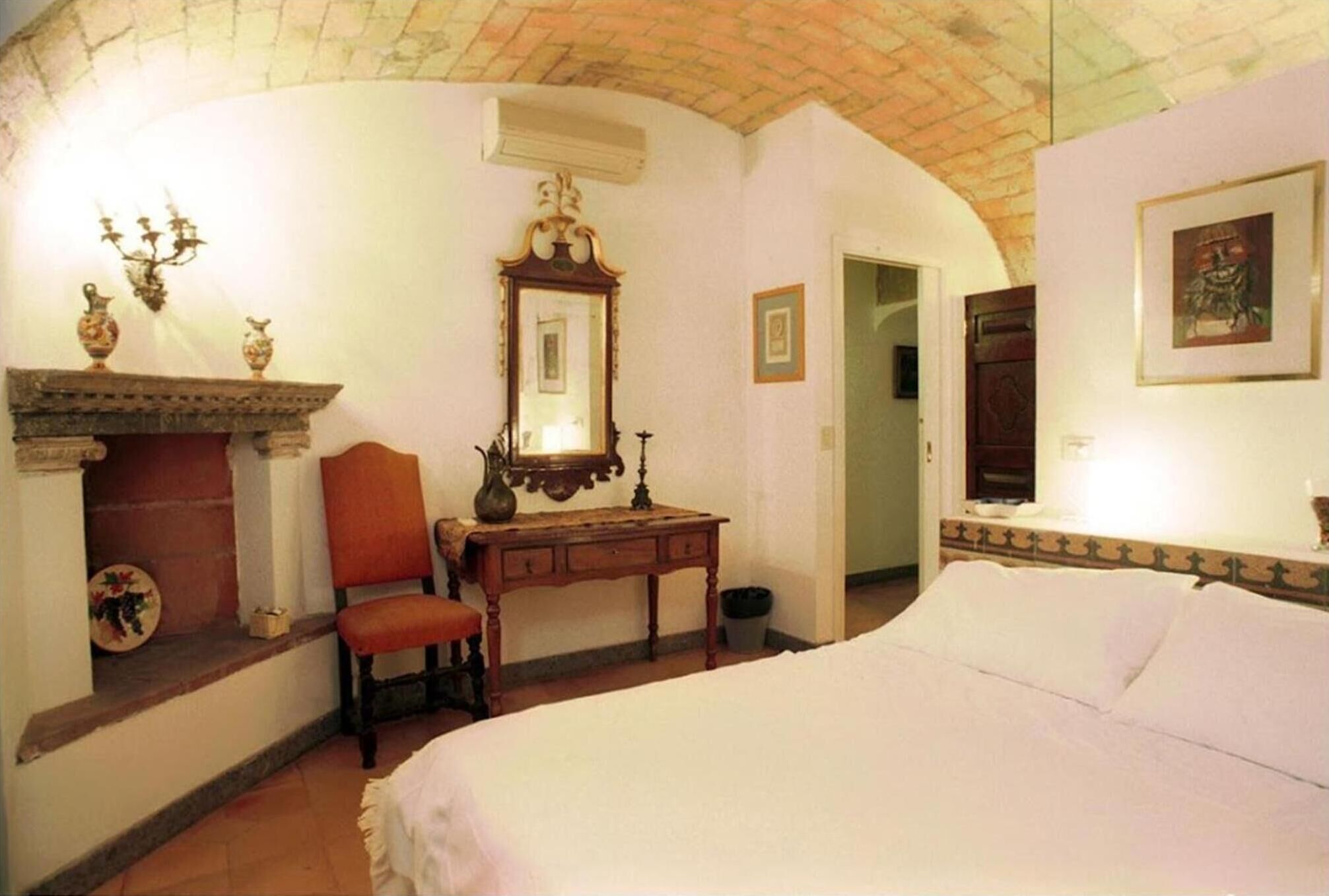 Un dormitorio con cama, escritorio, silla, chimenea y espejo.