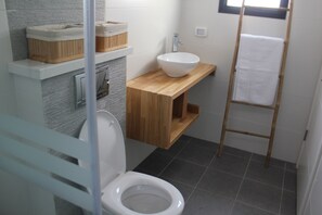 Et badeværelse med toilet, et træbord med vask og en håndklædestang.