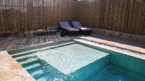 Une piscine rectangulaire avec deux chaises longues et une clôture en bambou en arrière-plan.