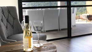 Une bouteille de vin blanc et deux verres sur une table en bois, dans une pièce offrant une vue dégagée grâce à de grandes fenêtres.