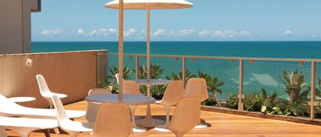 A deck with white chairs and tables, overlooking a clear blue sea.