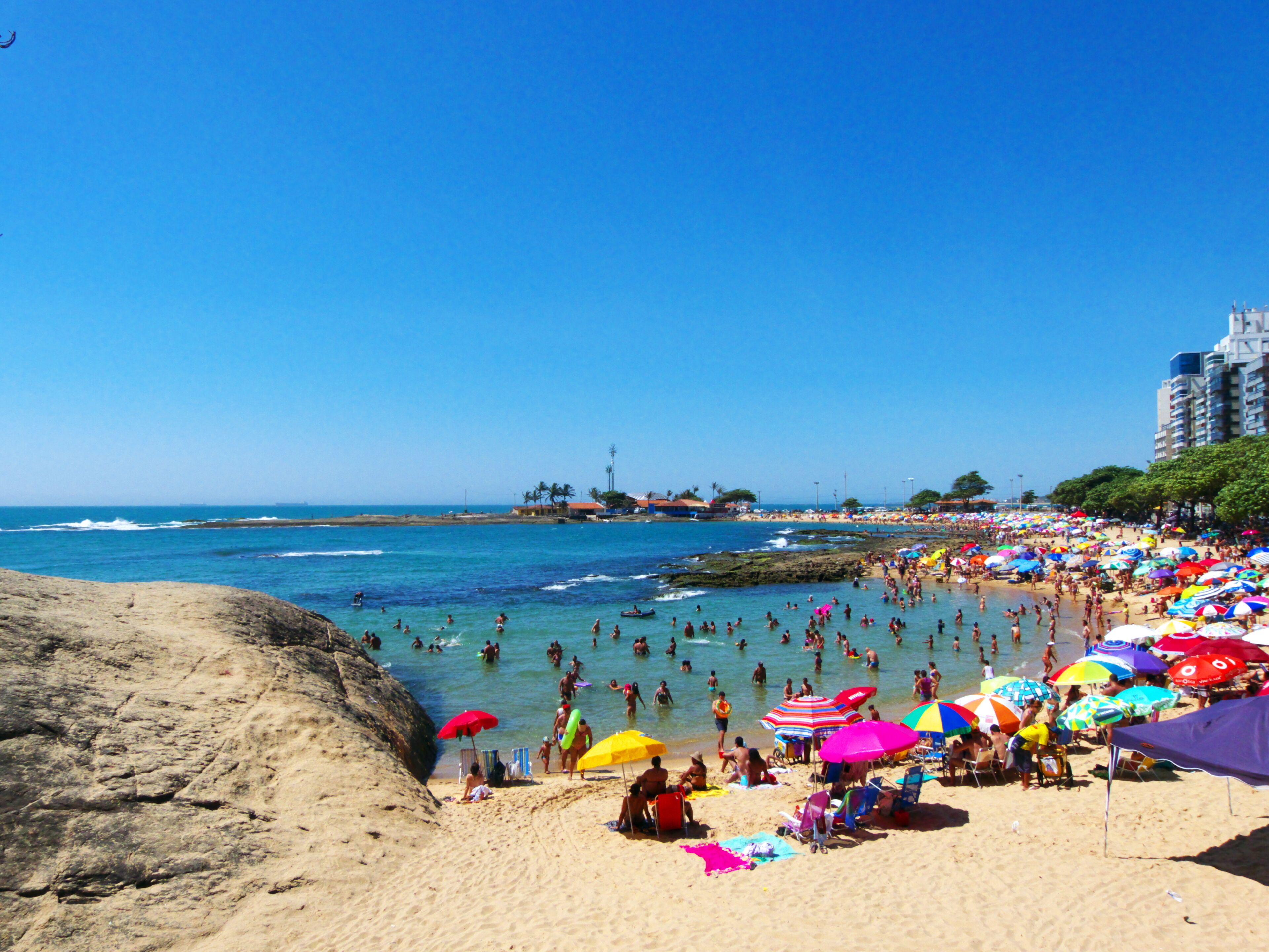A crowded beach with people swimming and sunbathing, and colorful umbrellas.