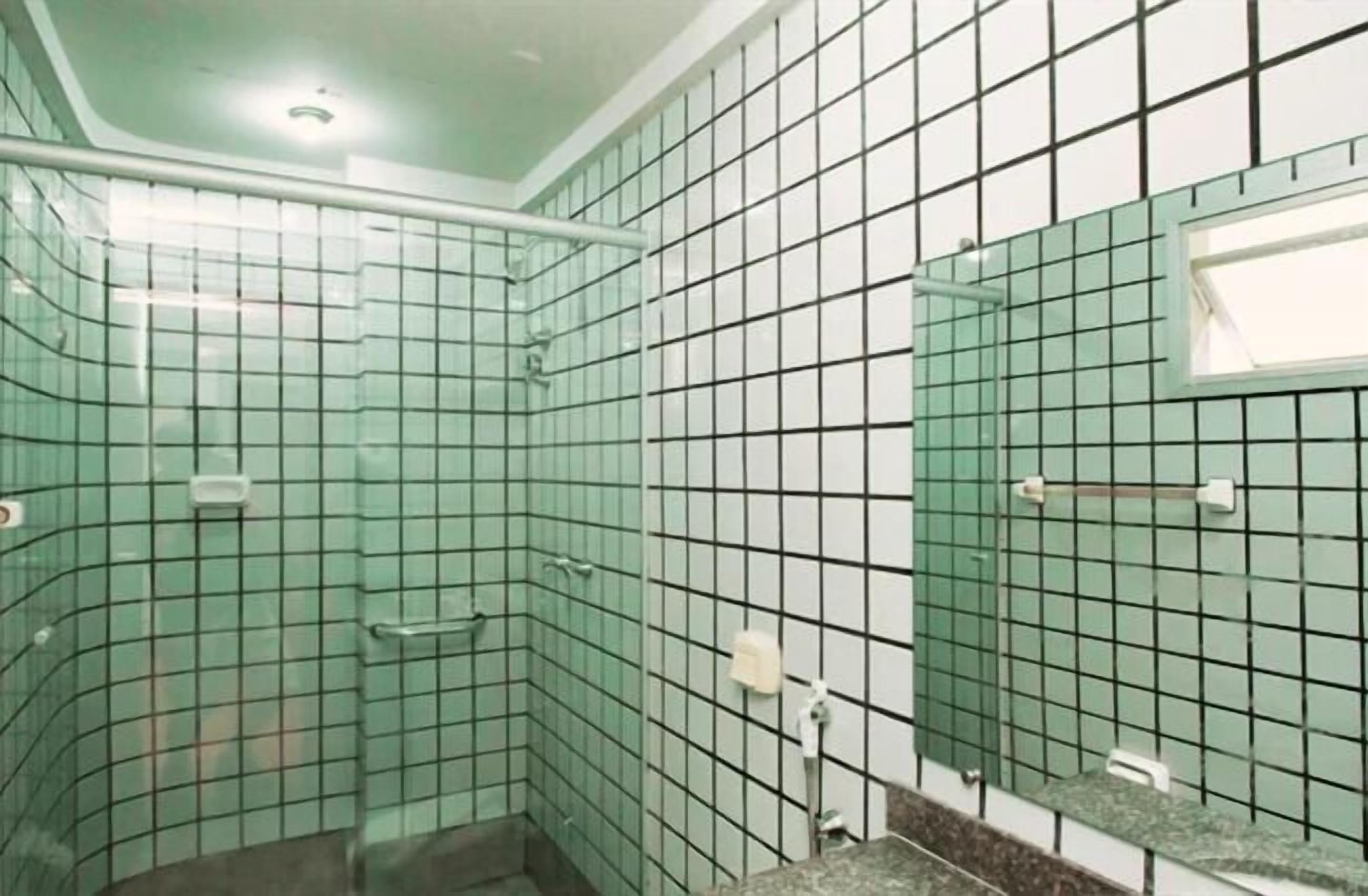 A bathroom with a tiled floor, a shower area, a sink with a mirror, and a toilet.