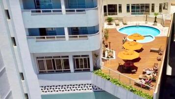Un edificio de varios pisos con una piscina en la azotea, zona de estar al aire libre y vistas a la piscina.