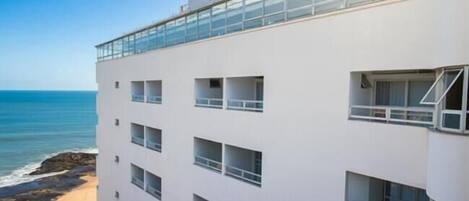 A multi-story hotel with balconies, a beach view, and a clear sky.