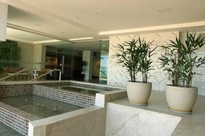 Un espace piscine intérieur moderne, doté d’un sol carrelé, d’un mur en verre et de deux grands plants en pot.