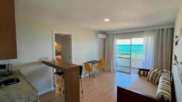 Una habitación con cocina, una mesa de comedor con sillas, un sofá con vista al mar y un ventanal grande.