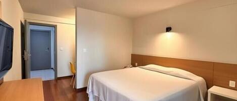 A bedroom with a bed, a bedside table, a chair, a television, and a door.