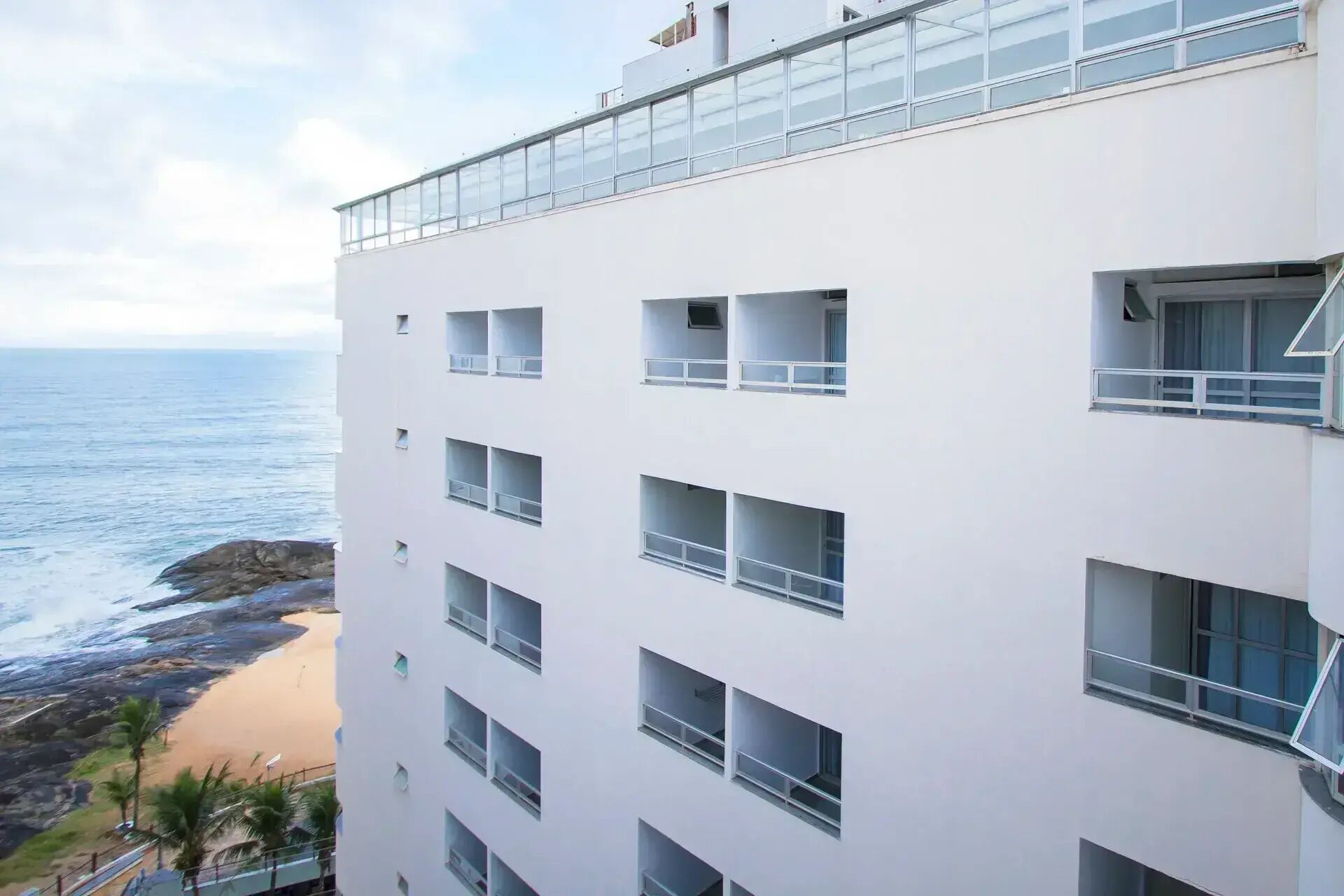 A multi-story building with balconies, a beach view, and a clear sky.