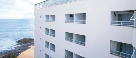 Een meerlaags gebouw met balkons, uitzicht op het strand en een heldere lucht.