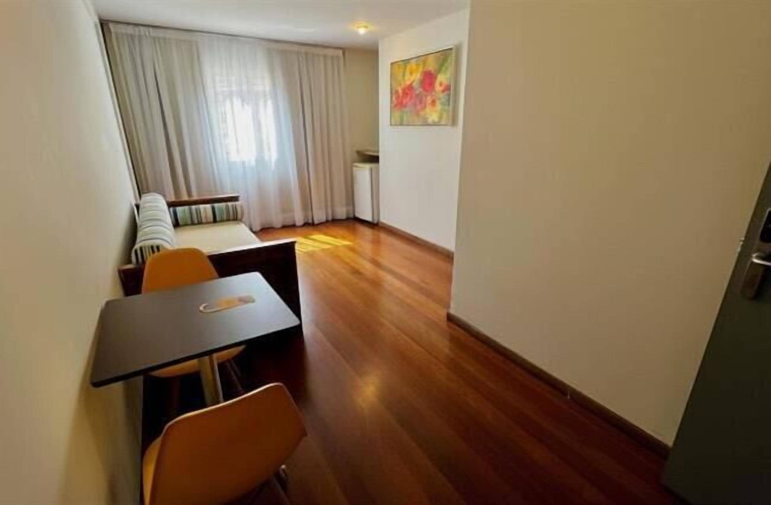 A room with a dining table, chairs, a sofa, a radiator, and a painting on the wall.