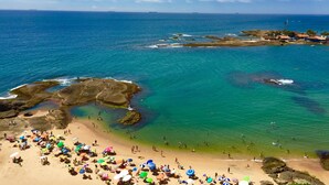 Une plage bordée d’une eau turquoise et limpide, de formations rocheuses et, au loin, d’une côte parsemée de bâtiments.
