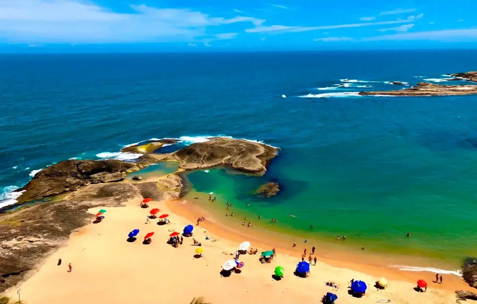 Una playa con agua cristalina, formaciones rocosas y gente disfrutando del entorno.