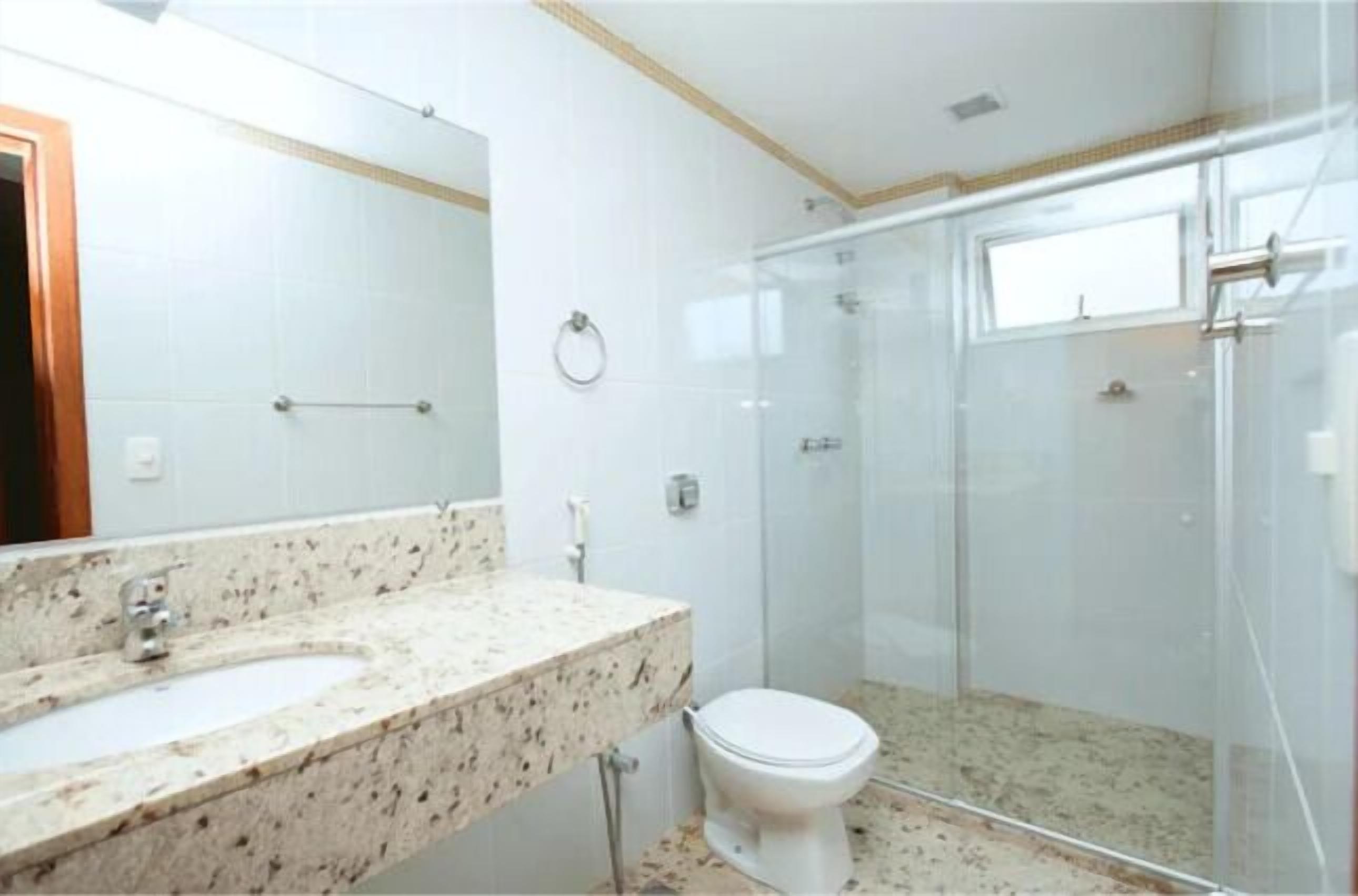 A bathroom with a marble sink, a toilet, and a glass-enclosed shower.