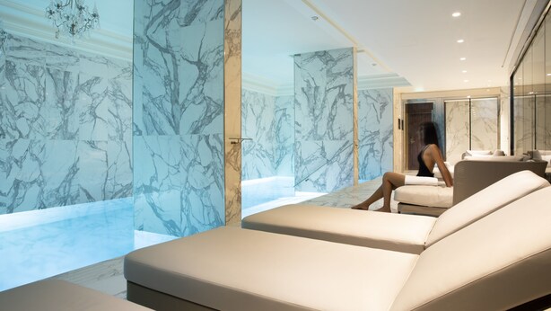 Un moderno espacio de spa con paredes de mármol, una bañera grande y dos sillones de descanso.