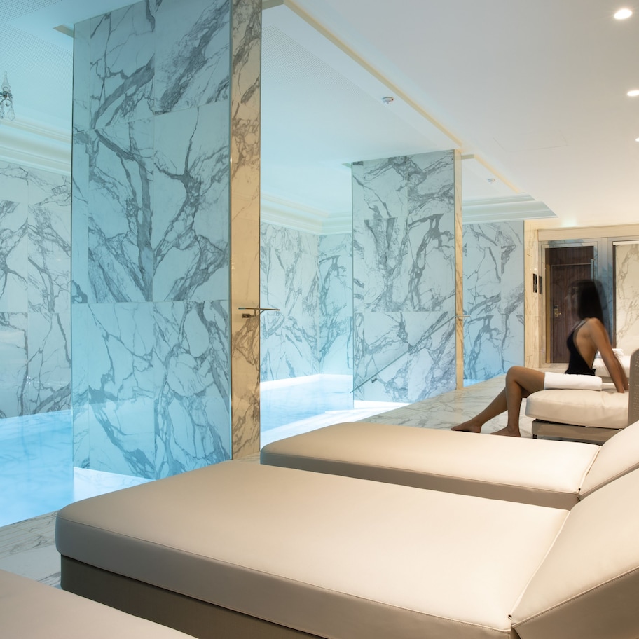 A modern spa area with marble walls, a large bathtub, and two lounge chairs.