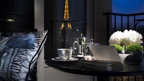 Una mesa con una taza, platillo, libro y objetos decorativos. Se ve la Torre Eiffel a través de una ventana.