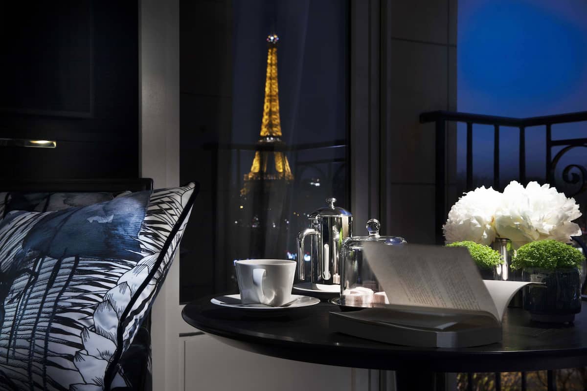 A table with a cup, saucer, book, and decorative items. A view of the Eiffel Tower is visible through a window.