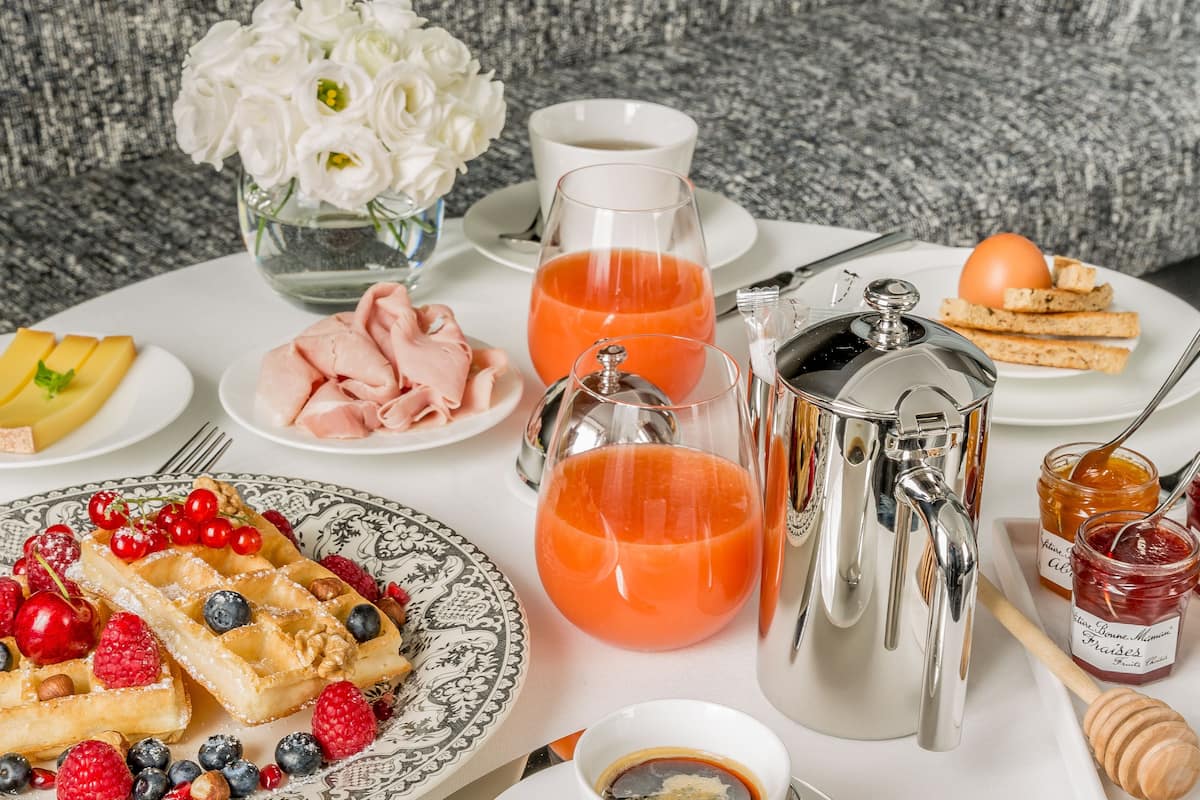 A breakfast setting with waffles, fruit, jam, and a coffee pot.