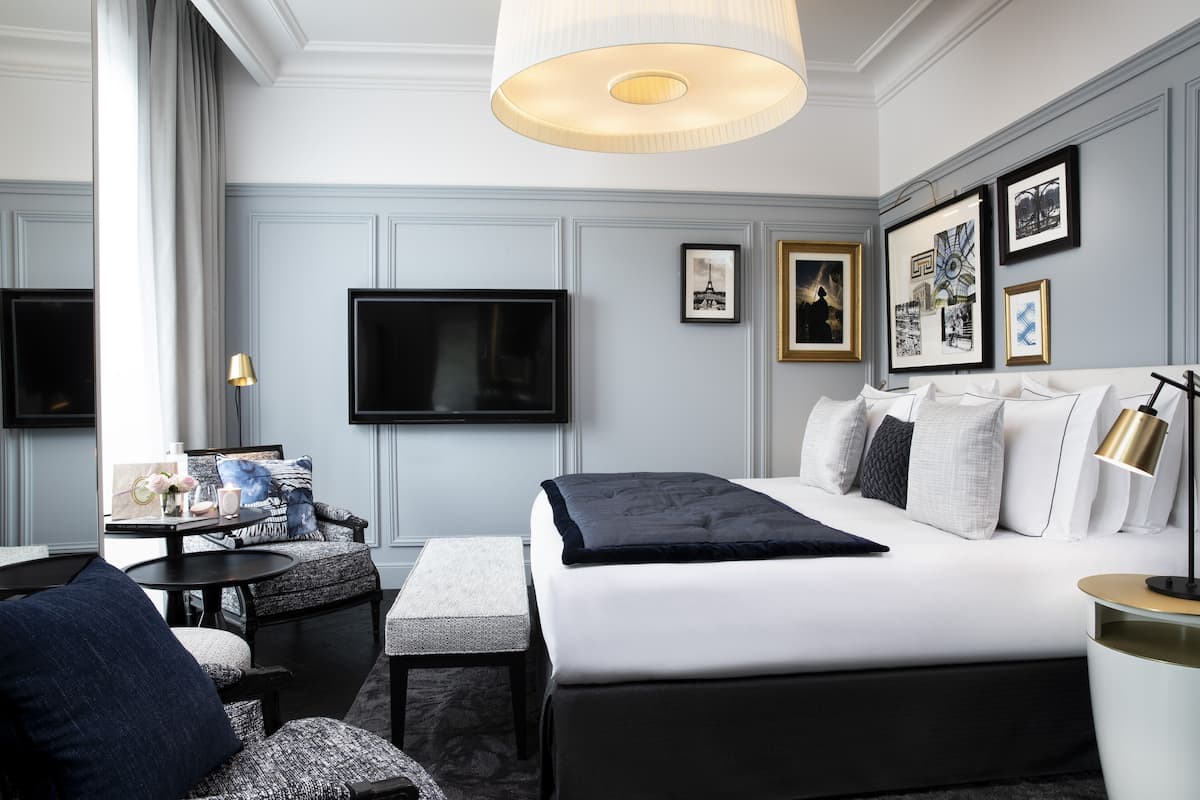 A modern hotel room with a large bed, a desk with a lamp, a TV, and framed pictures on the wall.