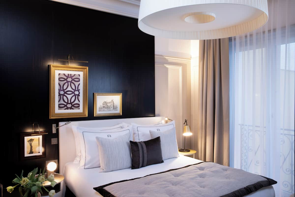 A hotel room with a large bed, bedside lamps, a wall-mounted artwork, and a view of the outdoors.