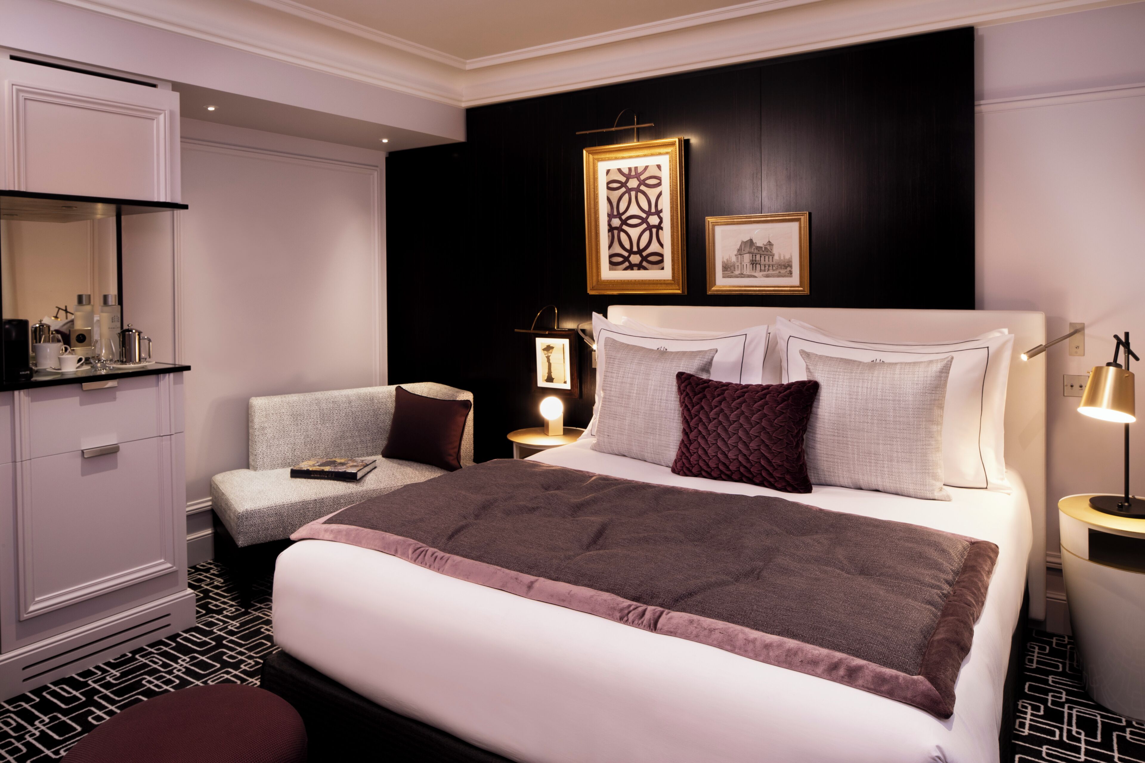 A hotel room with a large bed, a bedside table with a lamp, a chair, a wardrobe, and a mirror.