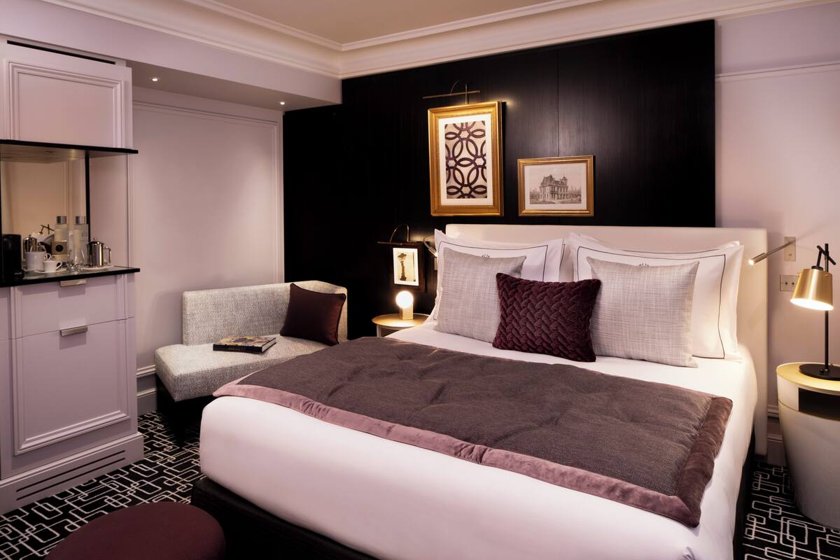 A hotel room with a large bed, a bedside table with a lamp, a chair, a dresser, and a mirror.