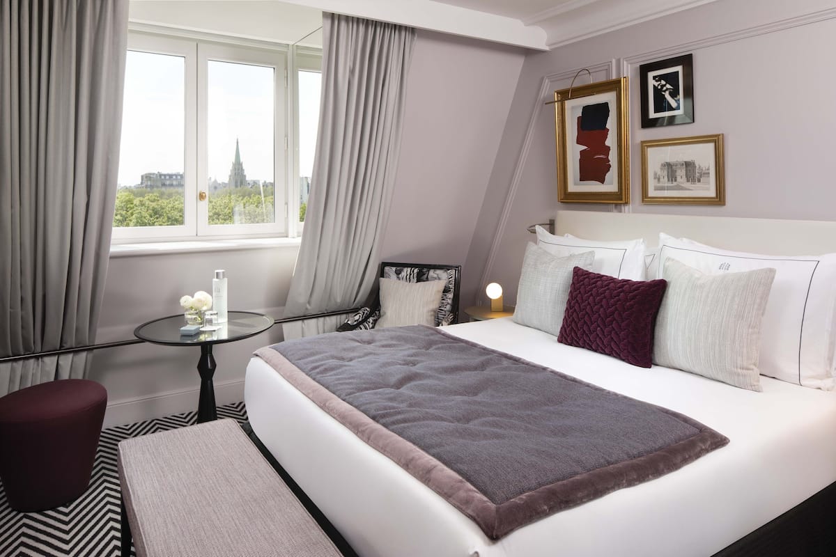 A hotel room with a bed, a round table, a chair, and a window with curtains.